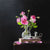 Autumn Rose by Alexander Volkov is a realistic still life of pink roses in a glass vase on a dark wood table, atop a closed book with scattered petals, and an old-fashioned inkwell nearby, creating a stunning contrast of light and dark.