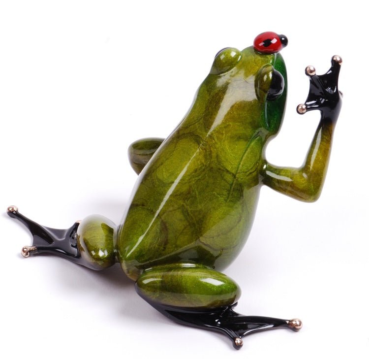 Bugsy, a glossy green ceramic frog sculpture with black feet, sits upright touching its face with a small red ladybug on its head. This intricately detailed Frogman art piece is available at Marcus Ashley Gallery and evokes the charm of Lake Tahoe.