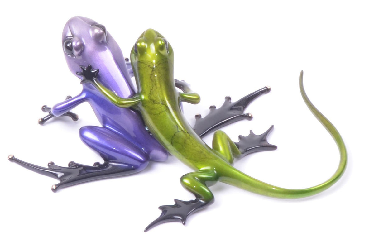 Two artistic metal lizards intertwined, one purple and the other green with exaggerated black feet. Reminiscent of Tim Cotterill art, Sidekick features a smooth, glossy finish on a white background, echoing the elegance of a Frogman sculpture.