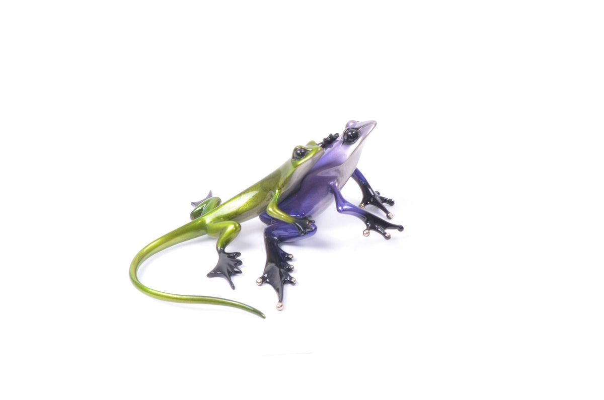 The Sidekick sculpture by Frogman (Tim Cotterill) features two vibrant glass frogs with striking black eyes and detailed limbs, set against a plain white background. Their glossy finish enhances the colors, echoing the classic appeal of bronze frogs.