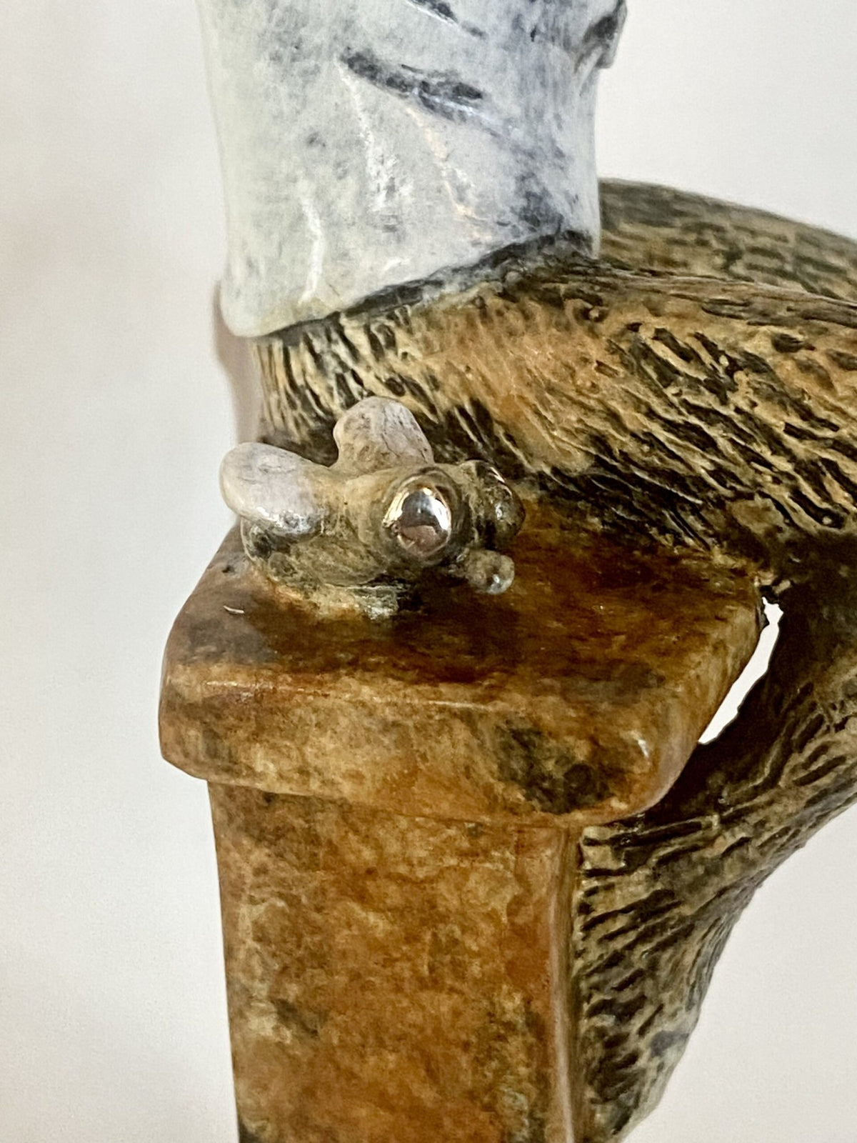 Close-up of Bar Fly, a small bronze sculpture featuring part of a figure seated on a textured bench with a sculpted fly, celebrating casual bar culture. Bronze, carved and painted.