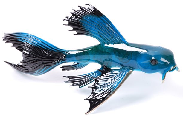 Big Blue is a blue and black ceramic fish sculpture with flowing fins and a glossy finish, reminiscent of an aquatic Frogman Bronze piece. It appears to be swimming, showcasing its stunning body and intricate fin designs.