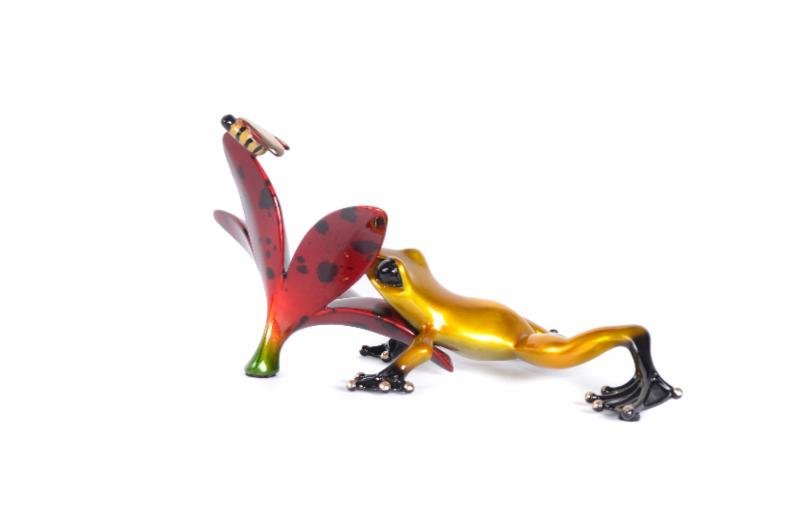 Buzz features a small, metallic-looking Frogman sculpture in gold and black, reaching for a red, spotted flower with a bee perched on top, all set against a white background. This piece epitomizes the enchanting charm of Tim Cotterill art.