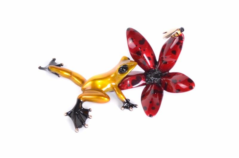 A small, colorful glass sculpture named Buzz, featuring a yellow frog with black feet and a vibrant red flower with black spots, reminiscent of Tim Cotterill art, set against a white background.
