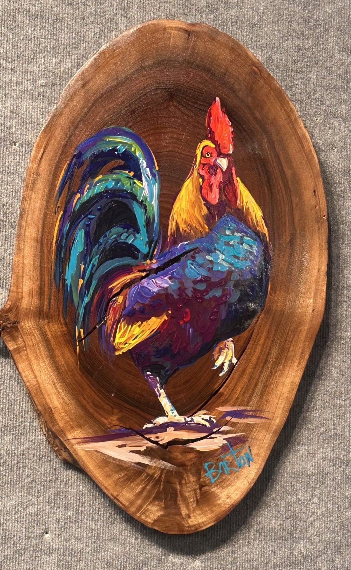 The painting Charlie features a colorful rooster on a live-edge wood slab, with vibrant red, blue, yellow, and purple hues. The natural wood grain enhances the artworks beauty, with Steve Bartons signature at the bottom.