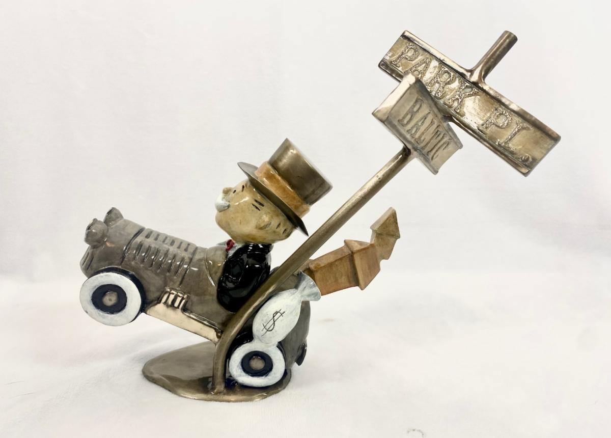 Paul B. Lotzs Highway To Hell is a small bronze sculpture of a figure in a top hat driving a vintage car, angled as if climbing with Park Pl and Boardwalk signs near the rear wheel, adding a playful touch.