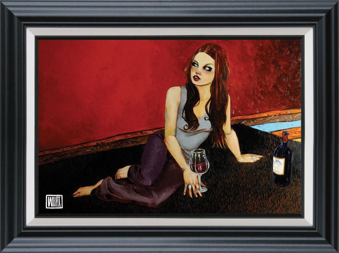 The limited edition painting Her Satisfied Place by Todd White depicts a woman with long brown hair lounging on a carpet, holding a wine glass, with a bottle nearby. It features a red-walled backdrop and window and is framed in black with a silver border at Marcus Ashley Fine Art Gallery.