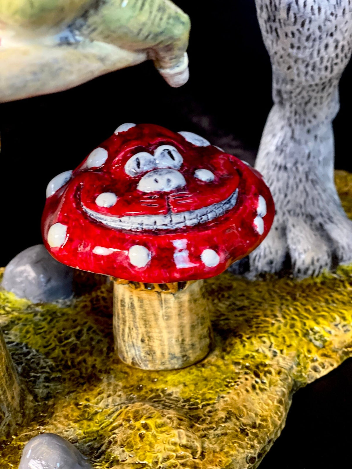 The White Rabbit sculpture features a red mushroom with white spots and a smiling face, surrounded by animal legs and mossy ground, creating a whimsical scene reminiscent of Alice’s adventures.