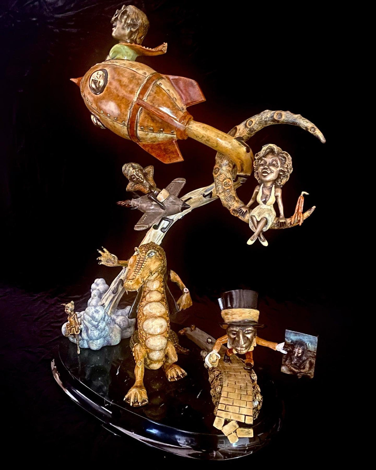 The whimsical bronze sculpture If I Was a Sculptor features a cartoonish rocket à la Rocket Man, topped by a child, with a dinosaur-like figure and abstract human faces, all set against a black background, capturing the imagination with its lively forms.