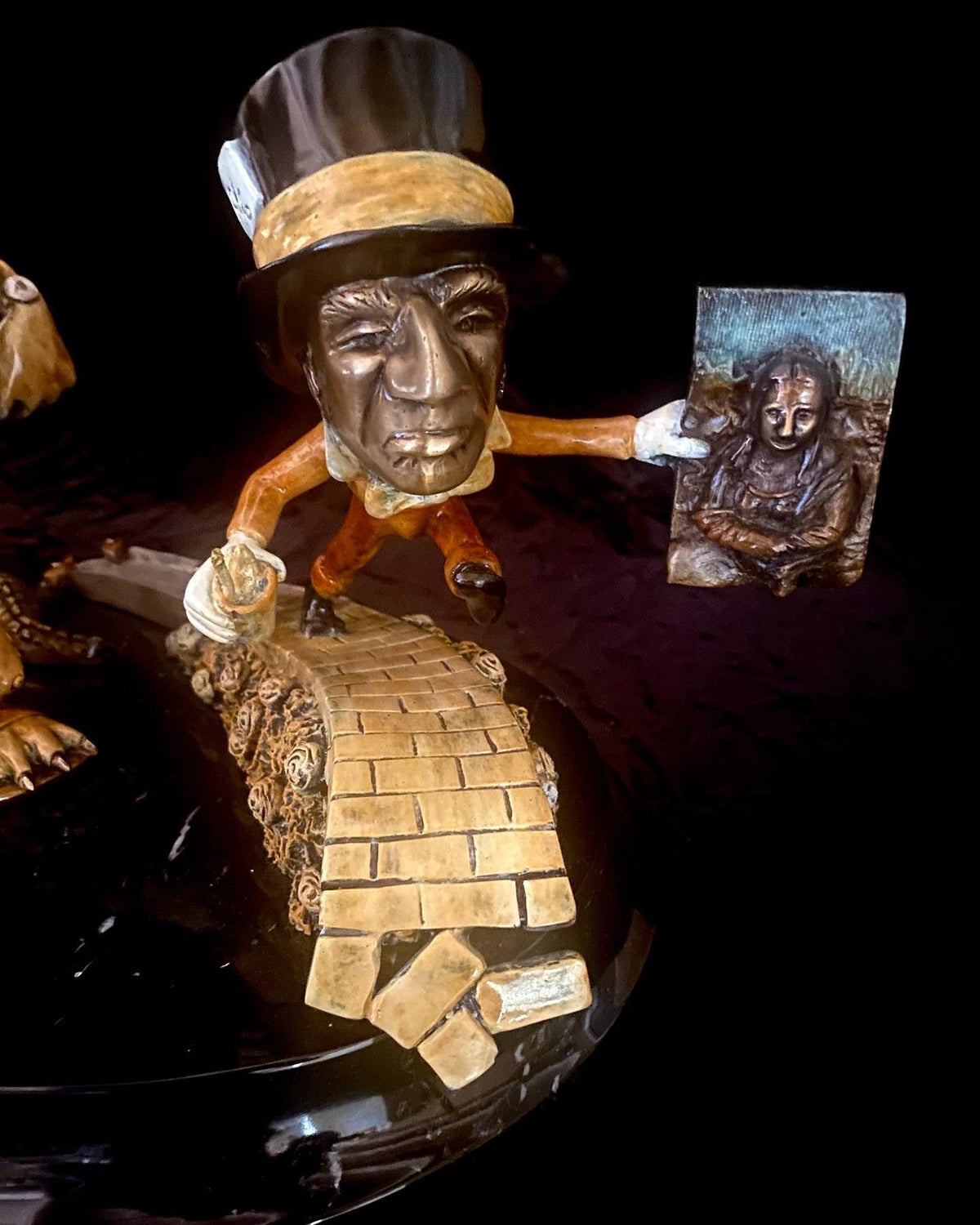 The If I Was a Sculptor figurine portrays an Elton John-like character with a black top hat and orange pants, standing on a yellow brick path. Holding a Mona Lisa painting, it creates an enchanting tableau against the dark background.