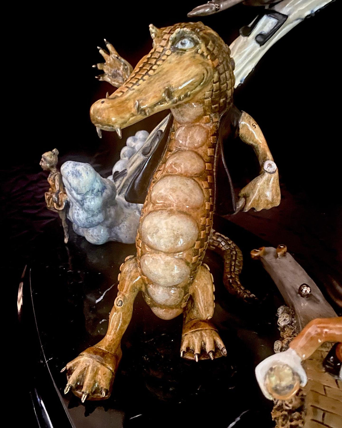 The bronze sculpture If I Was a Sculptor features a crocodile in a jacket standing upright, evoking Elton Johns flamboyance with its textured, scaly surface set against abstract, colorful shapes on a black glossy base, capturing the vibrant energy of Rocket Man.