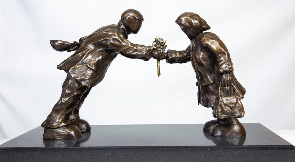 The bronze sculpture Leaning In For Love by Mackenzie Thorpe features two figures leaning towards each other with a bouquet and distinct clothing on a black base, capturing deep emotion and endless energy.