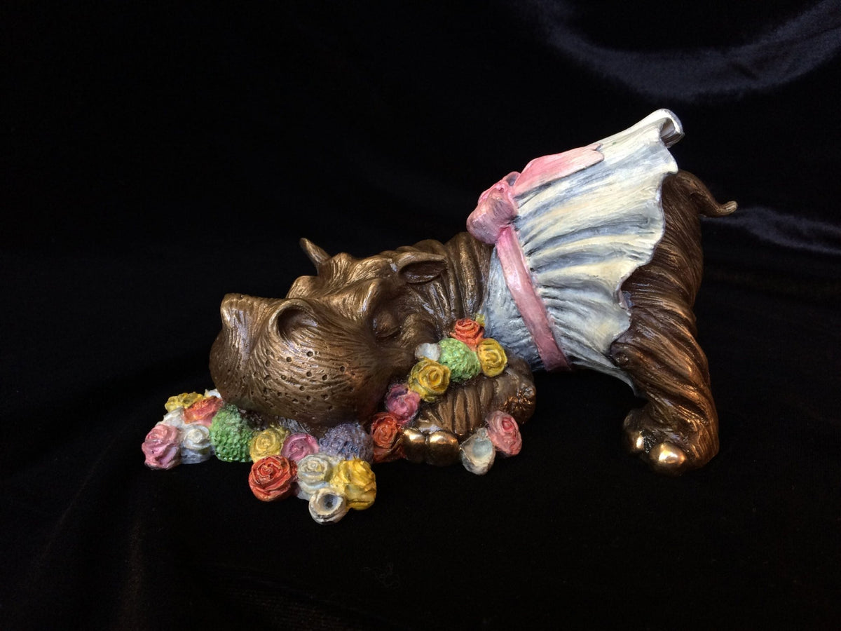 The Mary, Mary Quite Contrary sculpture is a delightful bronze piece of a playful dog in a dress, adorned with a colorful bouquet around its neck and paws. Pink and light blue flowers pop against the black background, reminiscent of nursery rhymes.