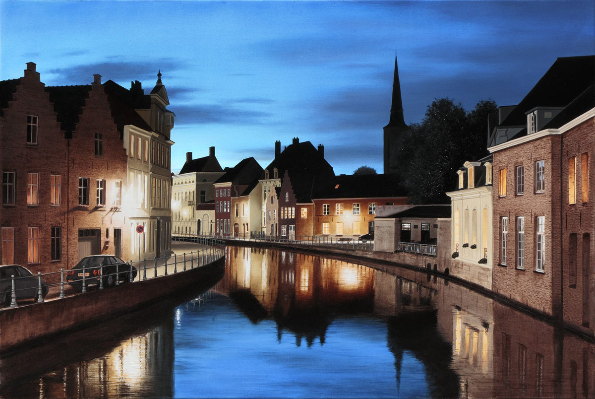 Nightfall in Bruges captures the scenic view of a canal at dusk, featuring historic brick buildings with lit windows reflecting on the water and a church steeple against a deep blue evening sky.