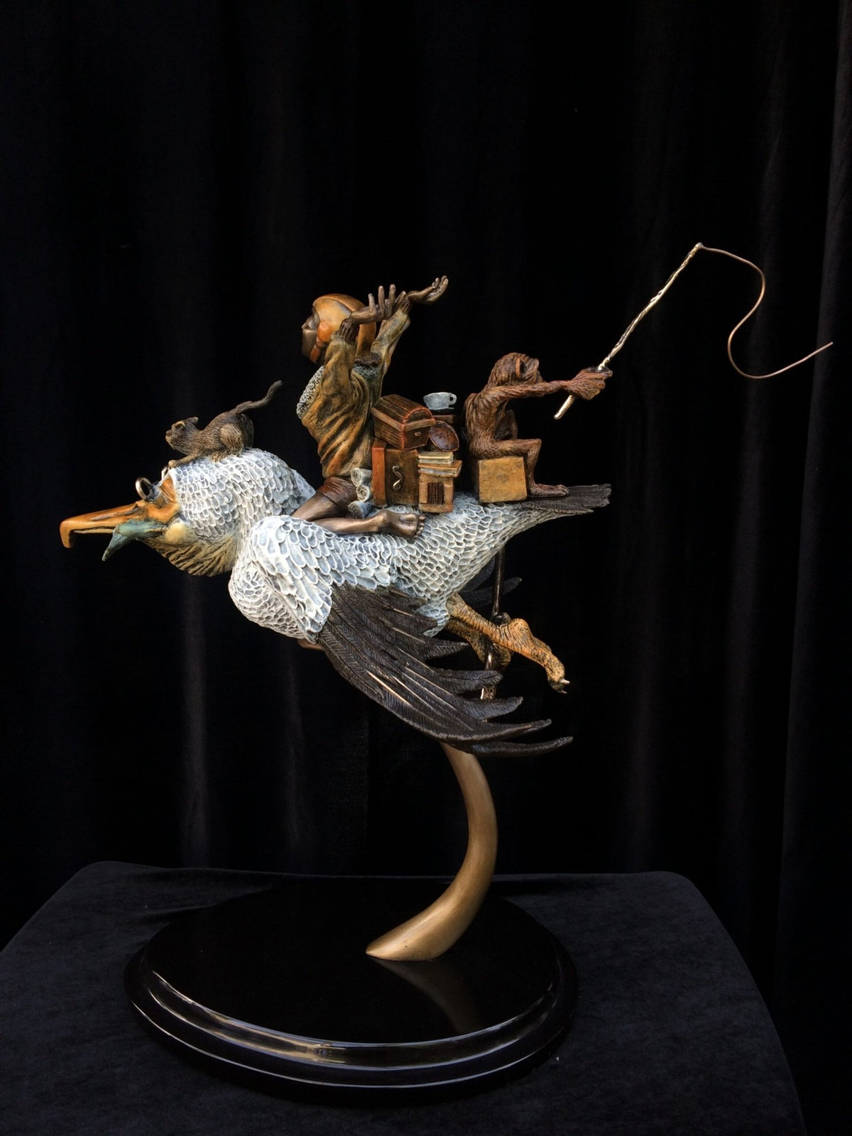 The Ode To Amelia Earhart bronze sculpture embodies adventurous spirit, depicting a bird in flight carrying a man with a saxophone and two monkeys, one gripping a fishing rod, all against a black backdrop, capturing the daring essence of Earharts legacy.