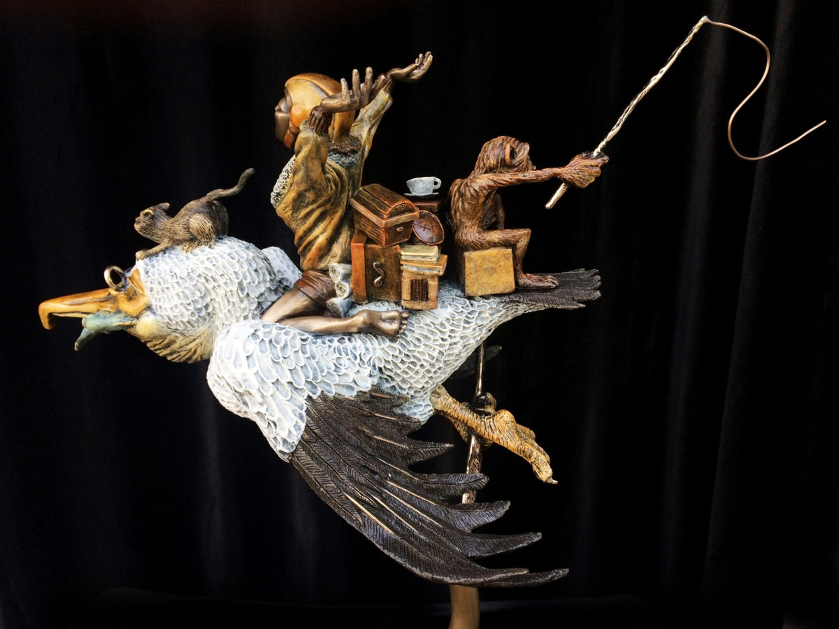 Sculpture titled Ode To Amelia Earhart features a bird with large wings carrying two human-like figures and objects against a dark background. One figure holds a stick aloft, echoing Amelias adventurous spirit, while a small creature sits at the front.
