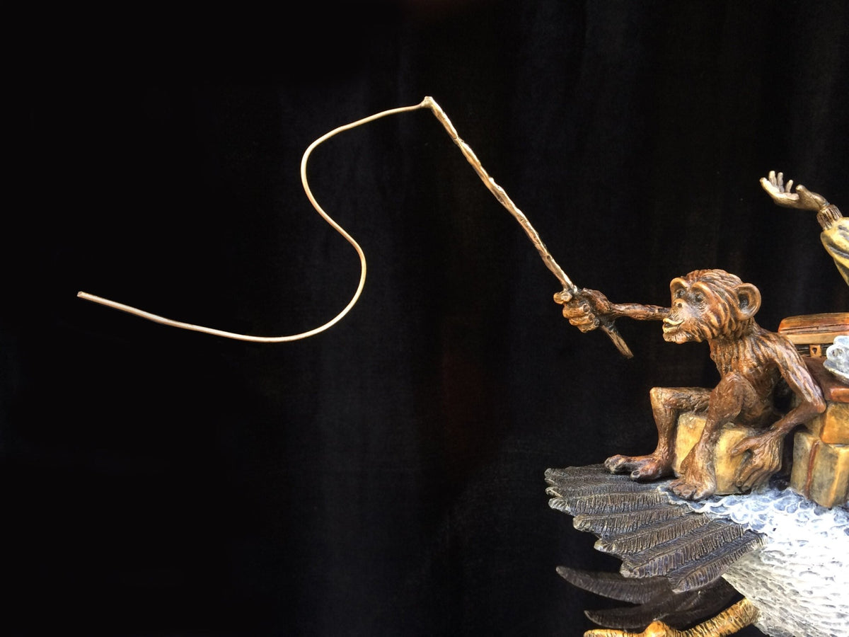 A detailed bronze sculpture portrays a monkey with wings, sitting on a rock and holding an upward-curved fishing rod against a black background. The focused monkey embodies the adventurous spirit present in Ode To Amelia Earhart.
