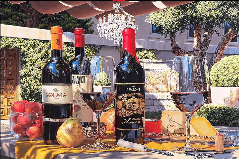 A sunlit outdoor table featuring Holding Court with two filled glasses, red and white grapes, European cheeses, and a pear is beautifully displayed. Above it hangs a chandelier, framed by trees and a building in the backdrop.
