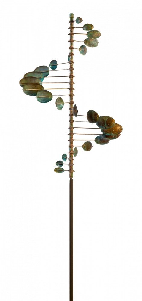 The Single Helix Oval is a tall, slender kinetic sculpture inspired by Lyman Whitakers work, featuring a vertical rod with horizontal metal arms. Each arm holds circular discs resembling leaves or sails in shades of green and bronze, elegantly forming an oval helical shape.