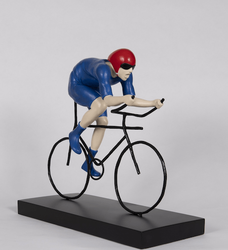 The limited edition bronze sculpture, The Fastest, depicts a cyclist adorned in vibrant blue attire with a red helmet, racing on a sleek black bicycle. It is mounted on a black base against a plain backdrop, capturing the dynamic spirit of the Tour de Yorkshire in Mackenzie Thorpes style.