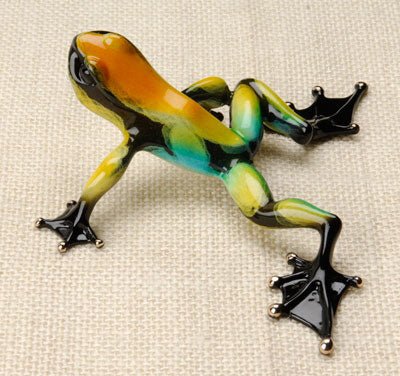 Zorro is a vibrant frog figurine with orange, yellow, green, and blue markings and glossy black feet, posed on textured beige fabric—capturing the lively artistry of Frogman Bronze.