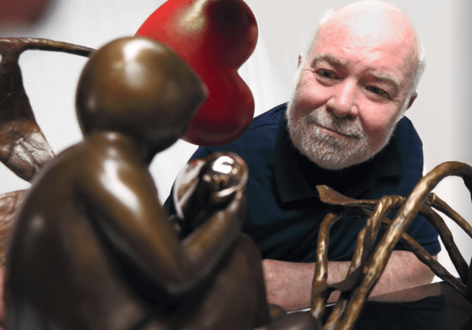 An older man with a white beard looks thoughtfully at All The Love In The World, a bronze sculpture featuring a human figure, heart shape, and organic forms at Marcus Ashley Gallery in the Lake Tahoe art district.
