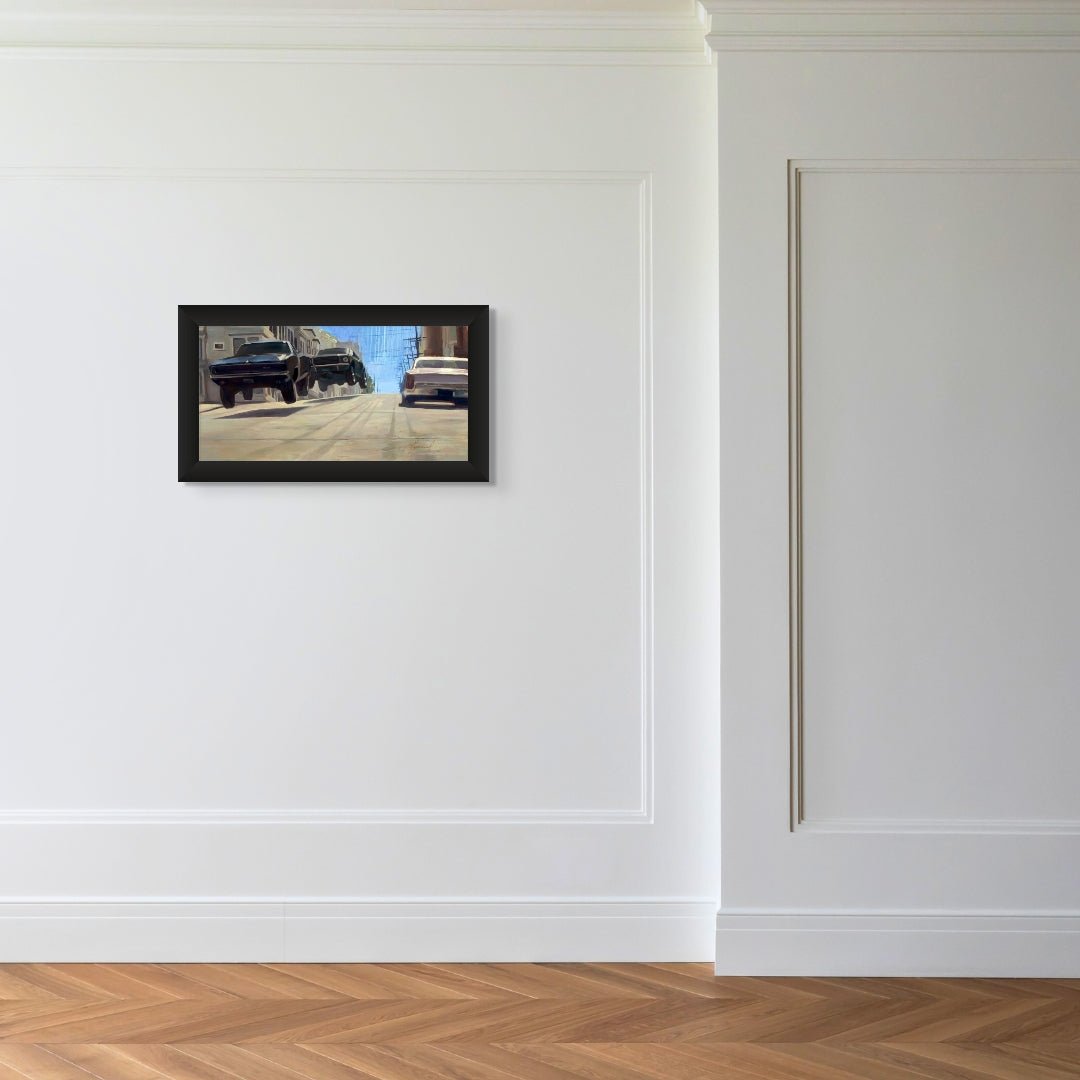 A minimalist room with white paneled walls and a wooden floor showcases a small framed picture of a street filled with vintage cars, reminiscent of Gabe Leonards Bullitt.