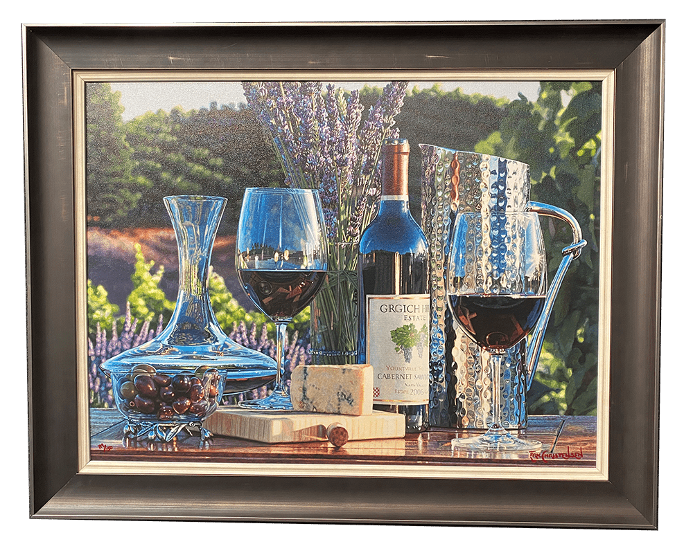 The framed painting Destination Napa by Eric Christensen captures a vineyard scene set against a lavender-filled backdrop, featuring two wine glasses, a bottle of red wine, a decanter, cheese block, grapes, and a metal pitcher on a wooden table.