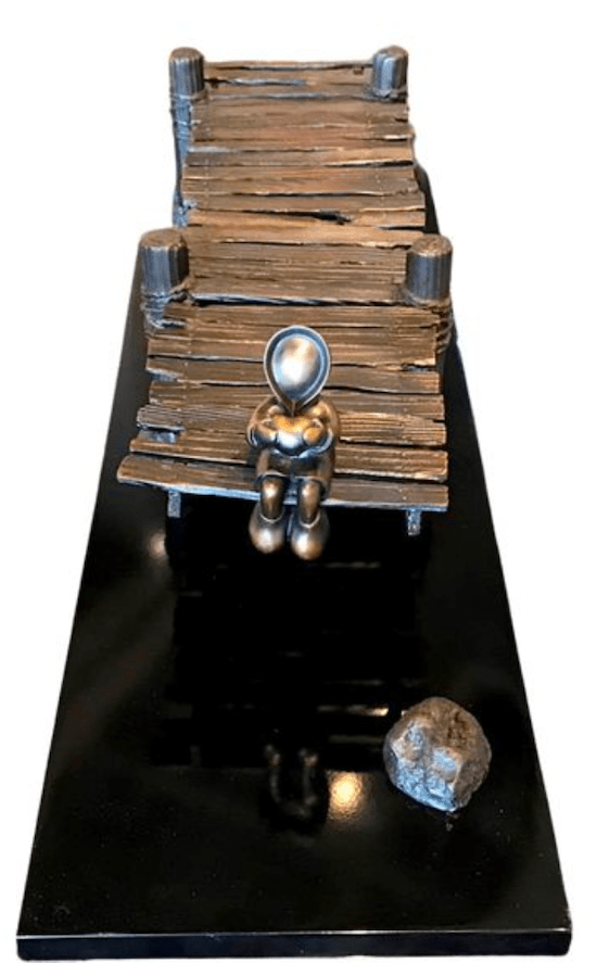The limited edition Dock of the Bay features a small bronze humanoid sculpture on a black rectangular base, echoing Mackenzie Thorpes style. It rests on a wooden dock with a nearby round stone, encapsulating solitude and contemplation.