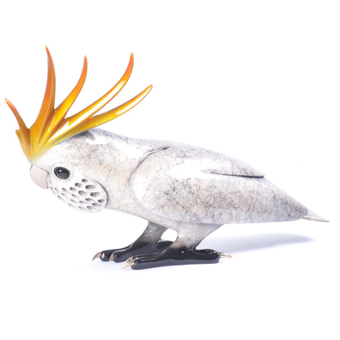 The Caruso sculpture portrays a cockatoo with a vivid orange and yellow crest, textured grey body, and black feet. It stands elegantly with its head angled left, showcasing detailed craftsmanship reminiscent of fine metalworks.