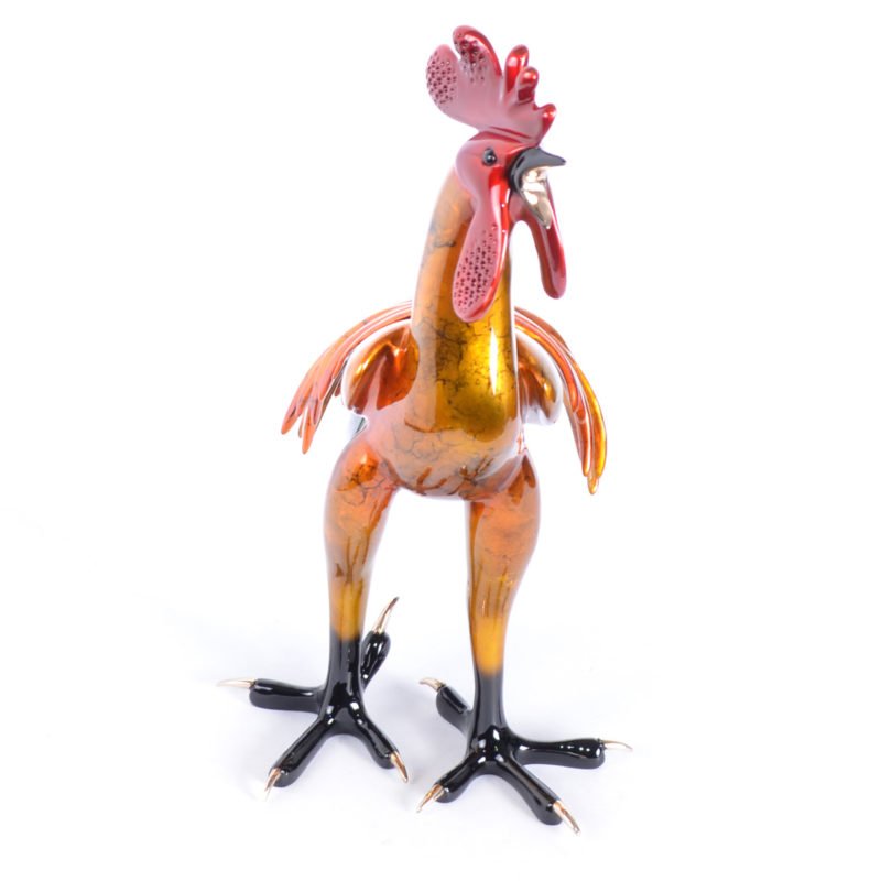 The Cocorico sculpture showcases a glass rooster with an orange and brown marbled body, black legs, and a red comb. Created using the Lost Wax casting technique, it features intricate details, a glossy finish, and stands elegantly against a white backdrop.