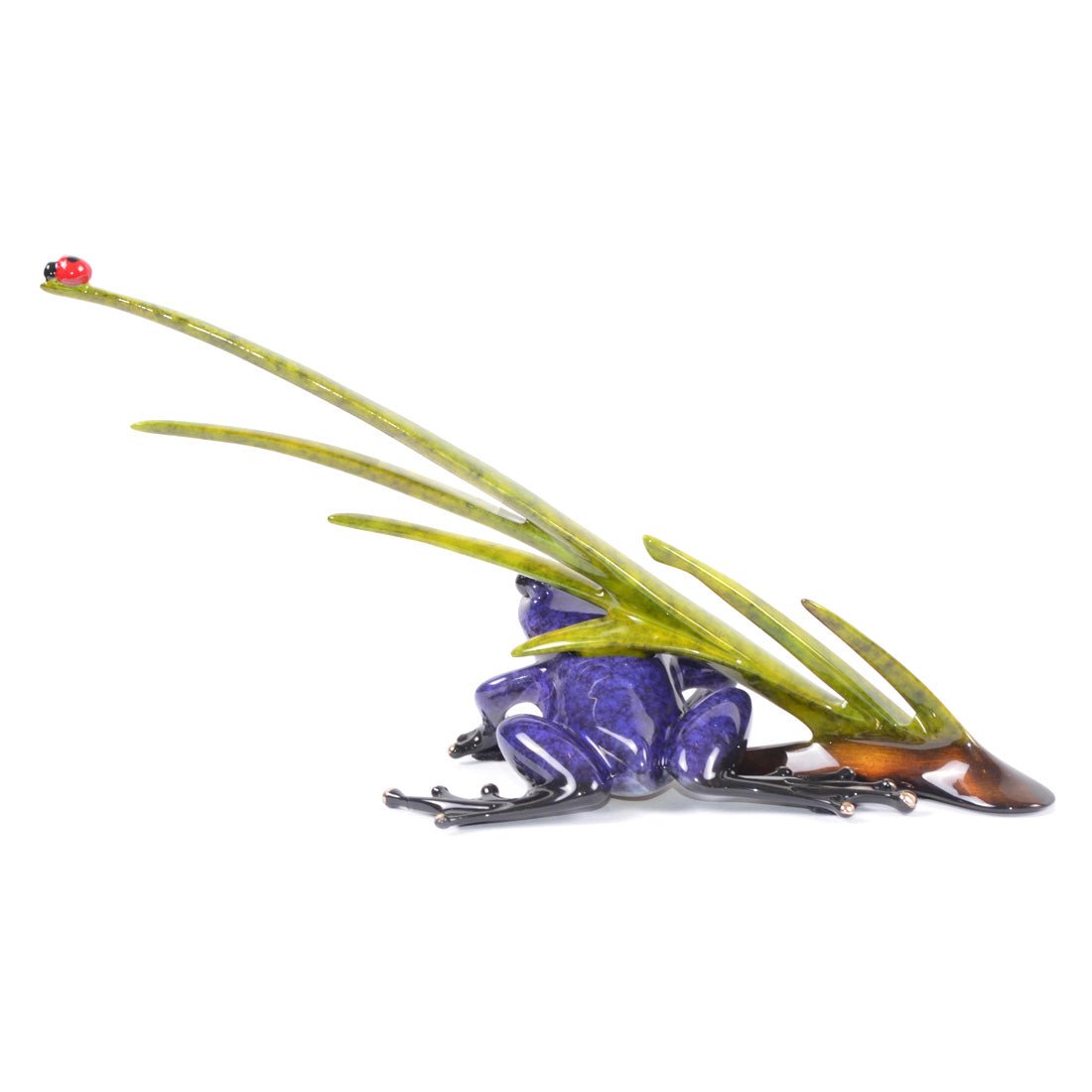 The Lookin for Love sculpture, inspired by Tim Frogman Cotterills art, features a purple frog with intricate details beneath long green leaves. A red ladybug rests on a leaf tip against a white backdrop.