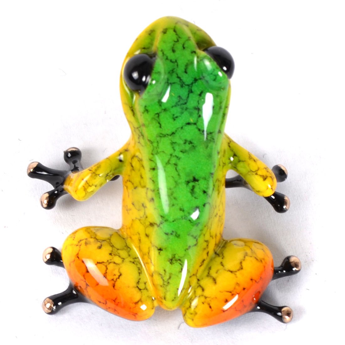 The glass frog figurine, named Salsa, mirrors Tim Cotterills whimsical Frogman art style. Its vibrant green body transitions to yellow and orange at the base with black toes. It sits elegantly on a white surface facing slightly left.