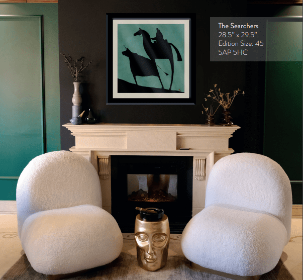 A contemporary living room showcases two plush white chairs, a black and gold fireplace, and a gold face-shaped side table. Above the fireplace hangs The Searchers, abstract art depicting black horses on a teal background. The green walls feature elegant accents.