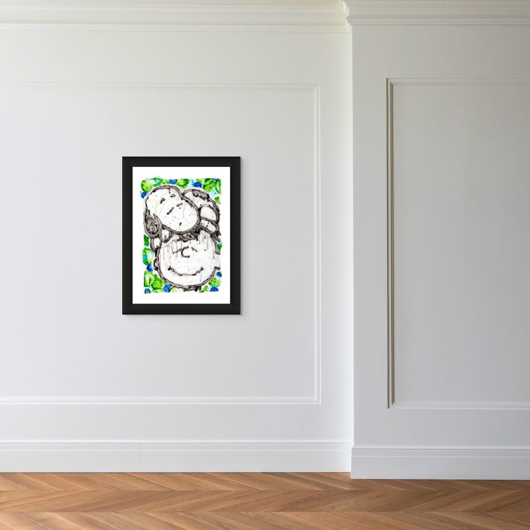 The framed Sleepover Homie Evening by Tom Everhart, with its vibrant green and blue accents that evoke childhood memories, hangs on a white wall. This captivating artwork enhances the serene minimal decor and wooden herringbone floor backdrop.