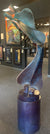 The Tango - Copper sculpture, with its sleek and abstract interlocking curves, rises from an 18 base. Surrounded by framed paintings in the art gallery, it captivates viewers, while the dim lighting enhances the contemporary ambiance.