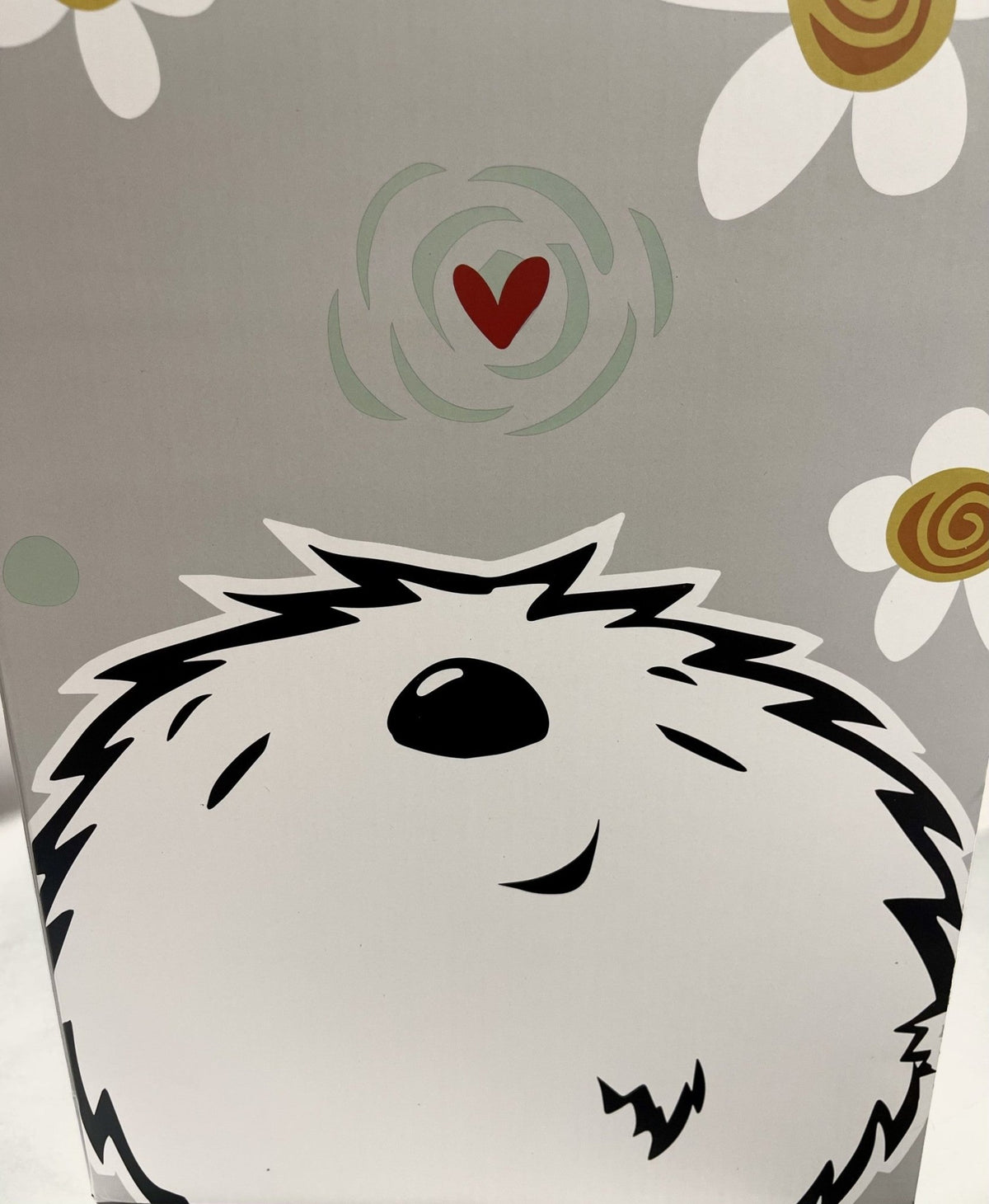 The Darwin Plush showcases a charming, stylized fluffy white dogs face with closed eyes and a black nose. Above it, a red heart with swirls echoes Fabio Napoleonis art style. White daisies with yellow centers on a gray background enhance its appeal, making it an ideal collectible piece.