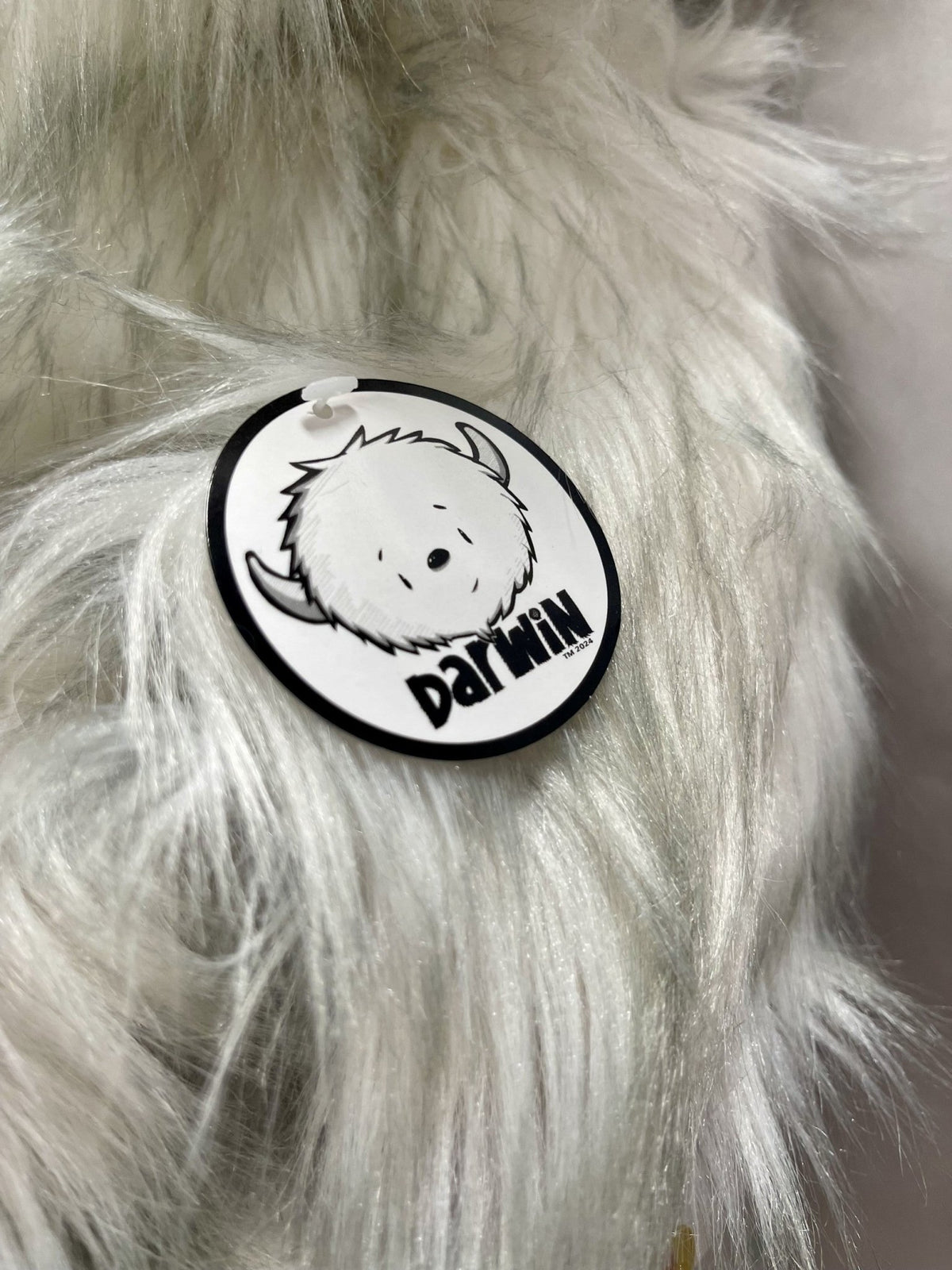 A close-up of the tag on a gray plush toy features a cute, horned creature and Darwin Plush in bold letters, capturing the essence of Fabio Napoleonis collectible box designs. Ideal for collectors.