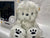 A plush white Darwin Plush toy with long, fluffy fur sits charmingly in front of its collectors box. It has black eyes, a small nose, and paw prints on its feet. The box showcases playful illustrations against a simple white background.