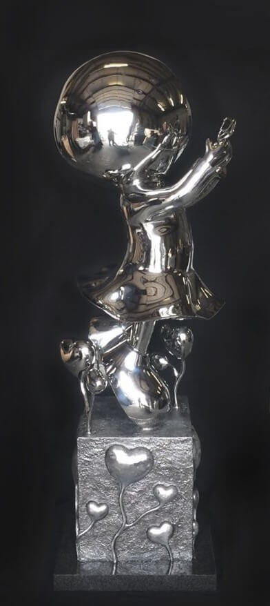 My Butterfly-Stainless” by Mackenzie Thorpe is a limited edition reflective metal statue featuring a stylized child with a large head, short dress, and holding an object. It stands on one foot atop a textured pedestal adorned with heart-shaped designs and small figures.