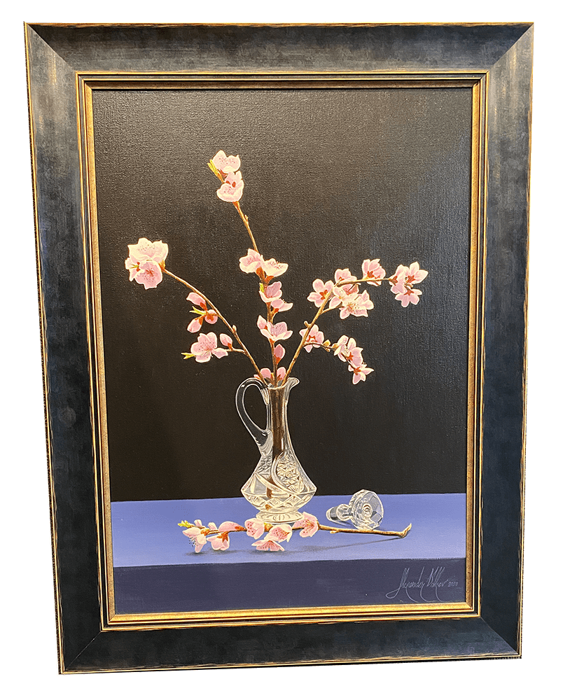 The framed painting Spring Cherry Blossoms by Alexander Volkov, available at Marcus Ashley Gallery, artfully depicts a glass vase with pink cherry blossoms against a dark background, with scattered blossoms on a blue surface enhancing its delicate beauty.