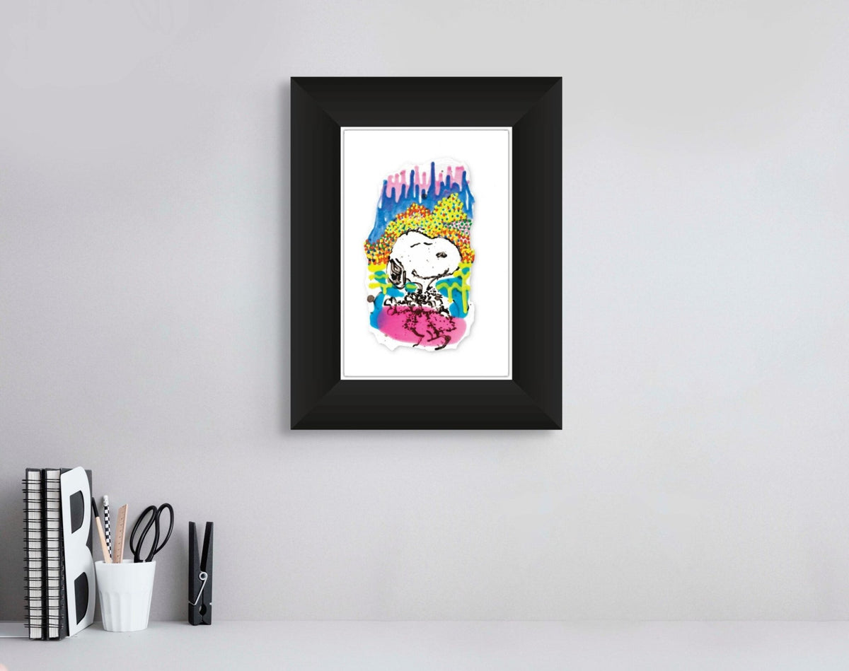 A framed illustration called Water Lilly IV, featuring a colorful pop art surreal owl with vibrant patterns, hangs on a gray wall above a desk that holds books, a vase with black pencils, and a decorative letter B.