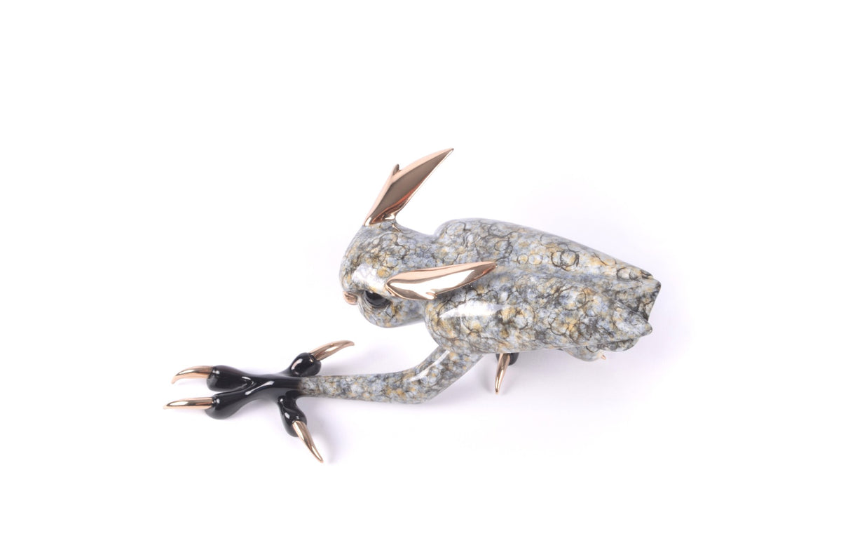 Zeus is a sculptural object resembling an abstract animal, with a speckled gray and gold-textured body, metallic gold ears and claws, glossy black segments on its front limb, and is set against a white background.